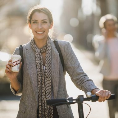 A young businesswoman drinking coffee during go to work with an electric scooter.