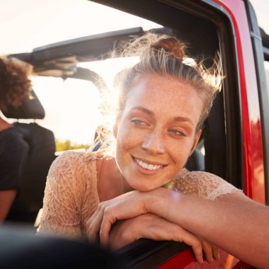 Millennial white couple on a road trip driving in open top car, women leaning on car door, close up
