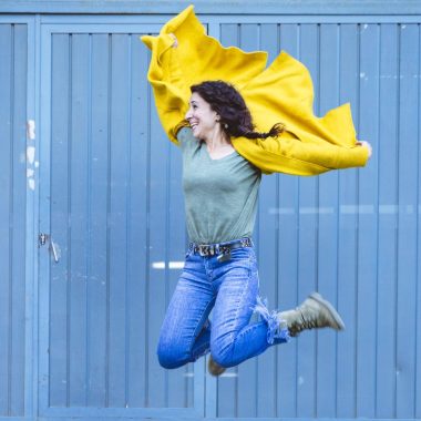 Woman in yellow coat takes a leap with a positive attitude in front of a blue door